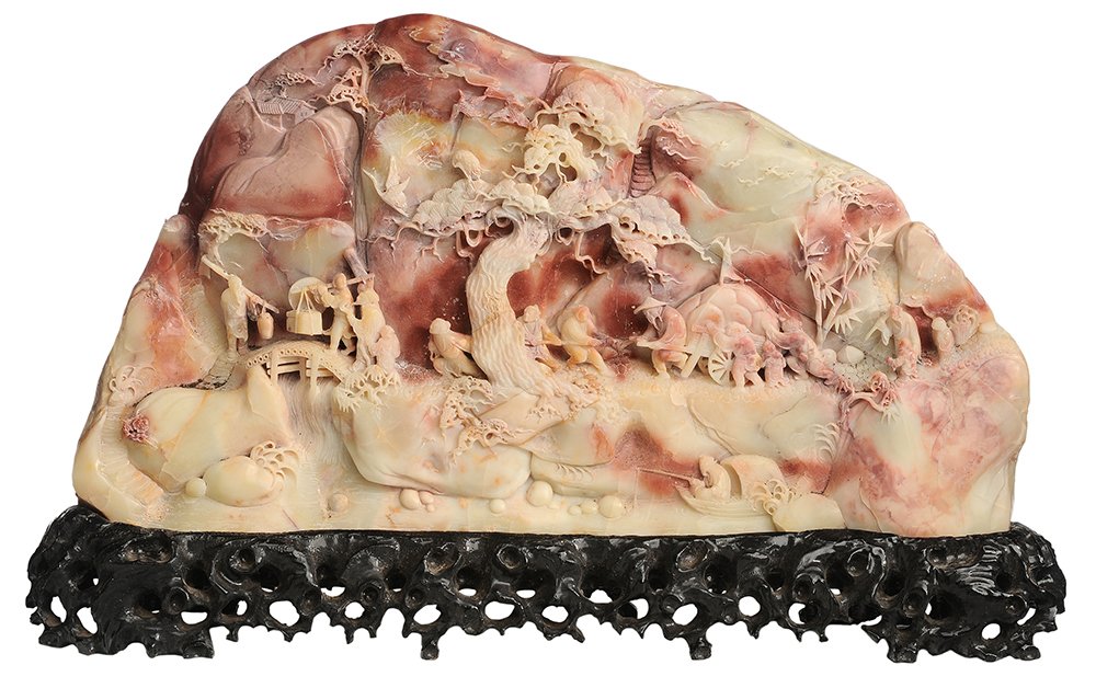 Finely Carved Soapstone Boulder: Chinese, 20th century, depicting a procession of figures with a prunus tree in foreground, carved on front only, dark salmon to ivory color, 11-1/4 x 20-1/2 in., carved wooden base, surface scratches 
