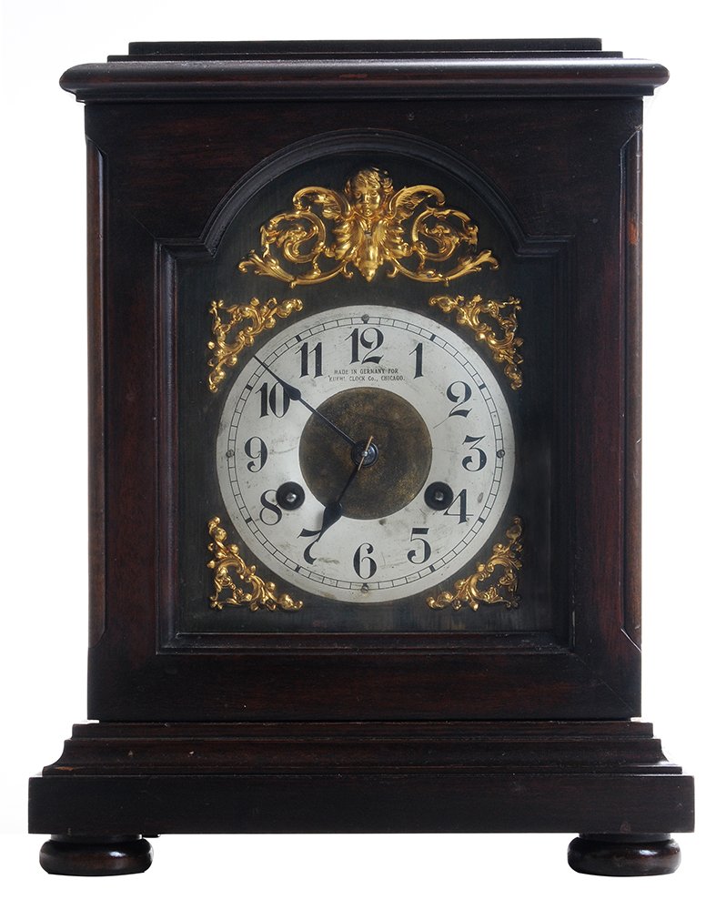 Mahogany-Cased Eight-Day Kuehl: Bracket Clock German, early 20th century, stepped flat molded top over a single door, enameled dial with Arabic counters and stamped "Made in Germany for Kuehl Clock Co., Chicago", brass surro