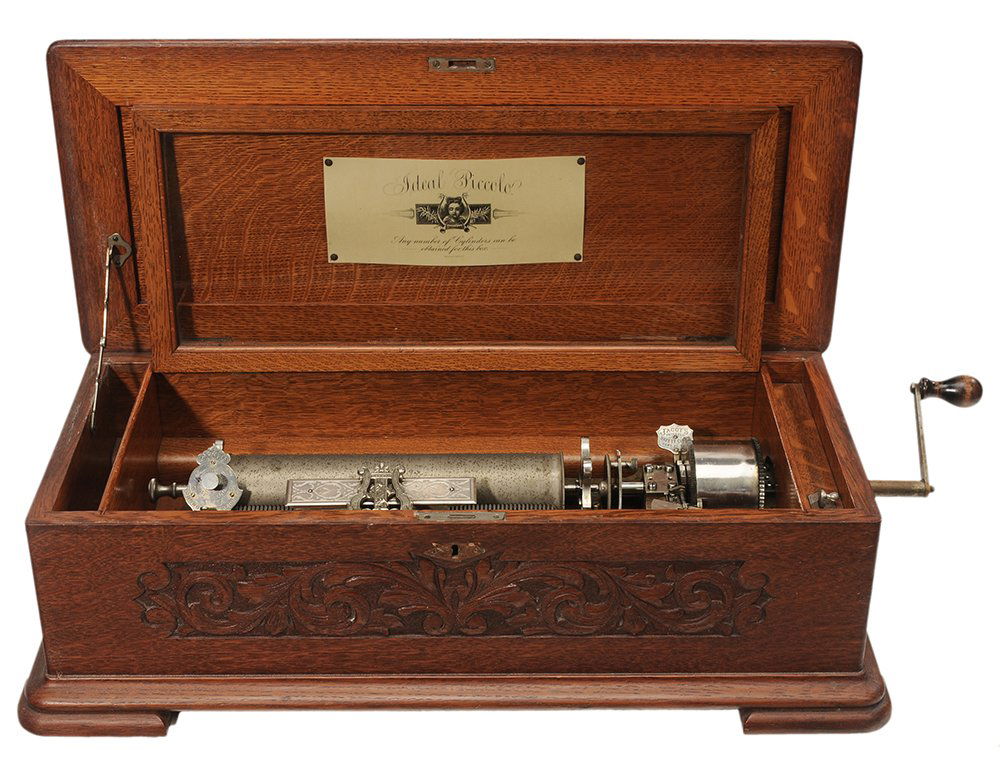 Jacot Patented Ideal Piccolo: Interchangeable Cylinder Music Box in Oak Case Swiss, late 19th century, paneled lift-top oak case, Jacot's Patent 1886 music box with interchangeable cylinders, winding crank, carved scrolling floral
