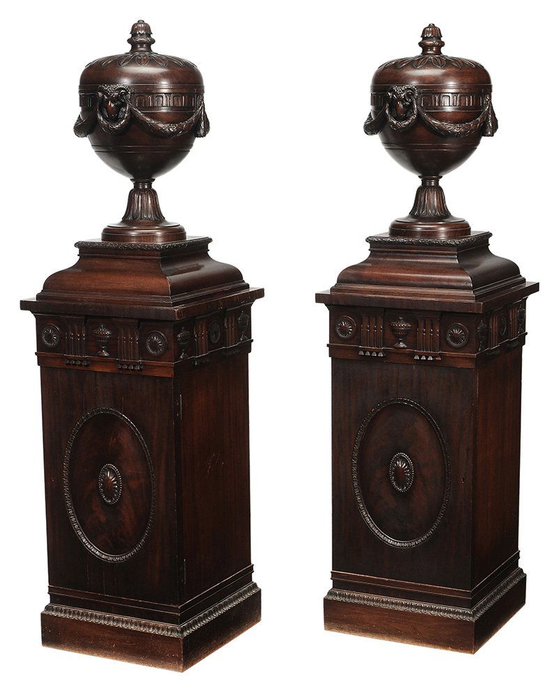 Pair Edwardian Mahogany Ram's Head and: and Swag-Carved Urns on Pedestals British, late 19th/early 20th century, urns carved from the solid piece of wood and with removable lids, stepped bases, pedestals with rosette and urn-carved friezes