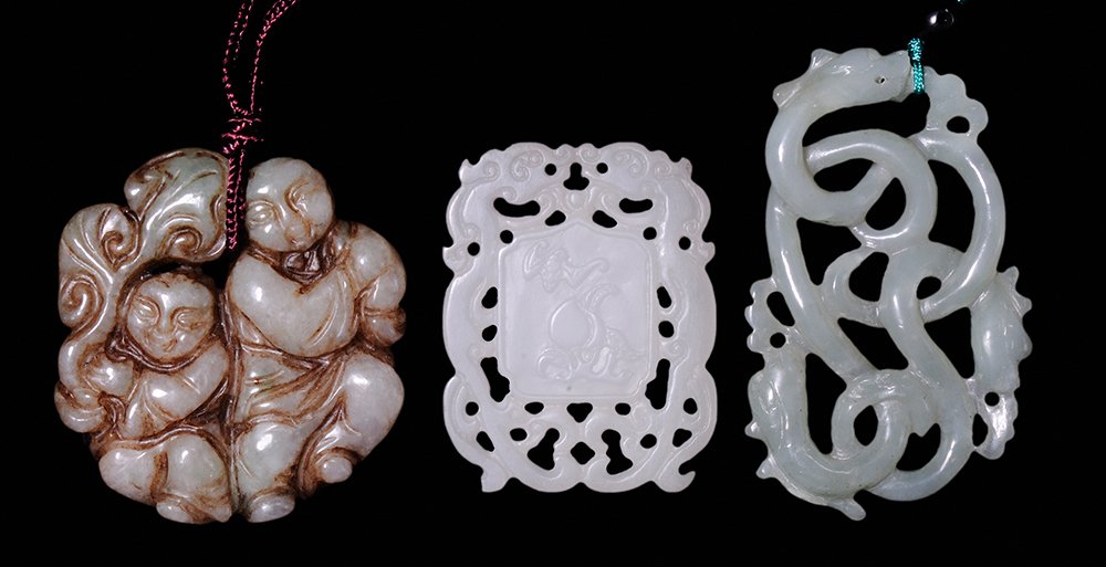 Three Chinese Stone Pendants: 20th century, jade carved and reticulated pendant decorated with Buddhist symbols on one side, stylized peach blossoms and branch with stylized bats, 1-3/4 in.; carved nephrite jade pendant depicting 
