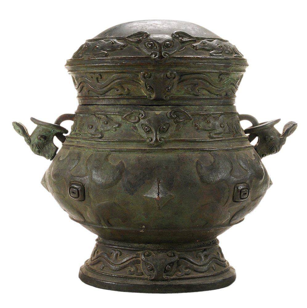 Zhou Style Bronze Covered Wine Vessel: Chinese, 20th century, cover with a water buffalo banded top centering an animal head, base with conforming band flanked by tilting water buffalo handles, stylized symbols and stars, conforming oval b