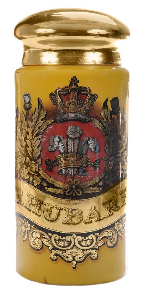 Very Large Reverse-Painted Glass: Tobacco Jar of cylindrical form with a domed gold cover, the body with gilt foliate scrollwork and banner with "RHUBARB" on mustard ground, overall height 24-1/2 in.,. Condition: some losses to paint,