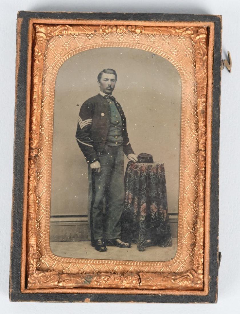 CIVIL WAR 1/8TH TINTYPE INFANTRY SERGEANT - TINTED: Beautifully tinted 1/8th plate tintype of a sergeant wearing what appears to be either a 1st corps badge or I.D. disk. His pants and vest are tinted sky blue. His kepi is resting on a table that is fe