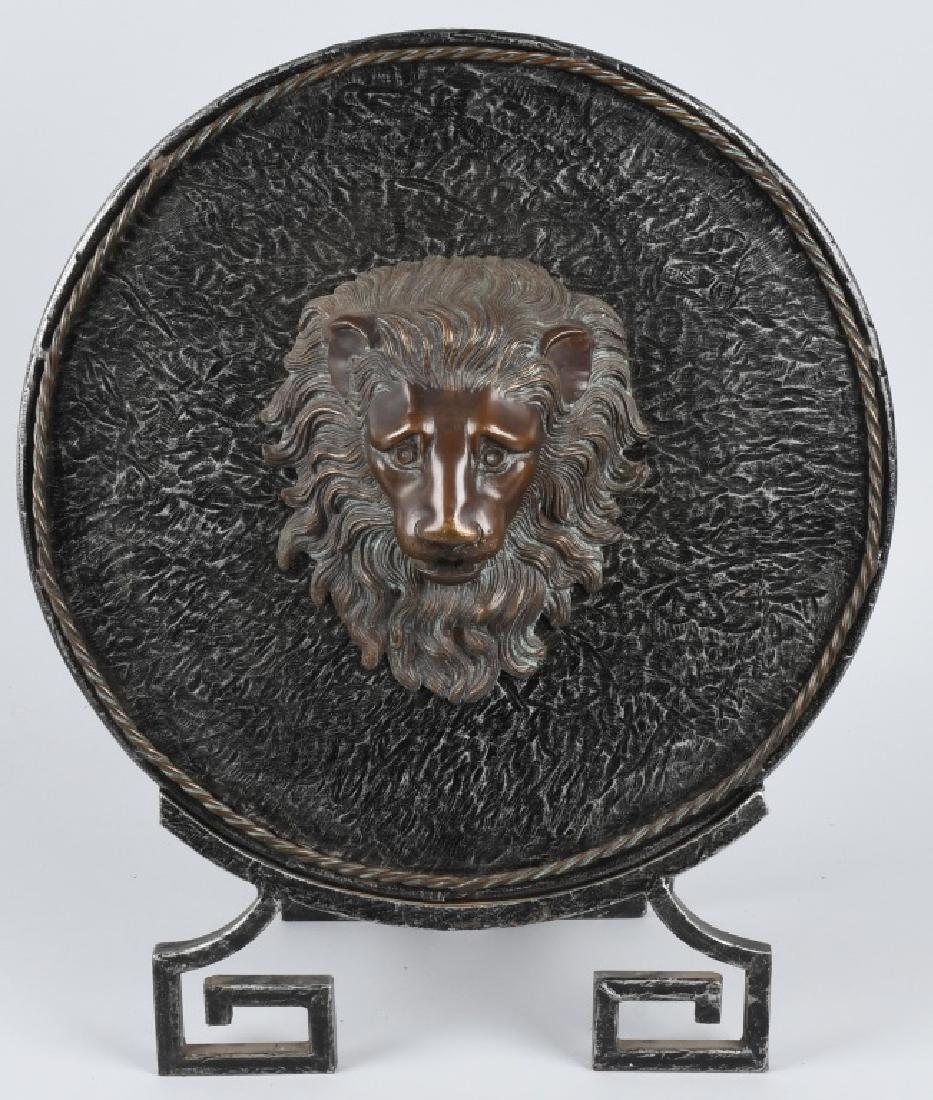 CAST ANDIRON SHIELD W/ BRONZE LION HEAD: Fabulous cast bronze lion head mounted on an iron shield with frame. There is a twisted bronze heavy wire around the edge. 20" by 17". Excellent