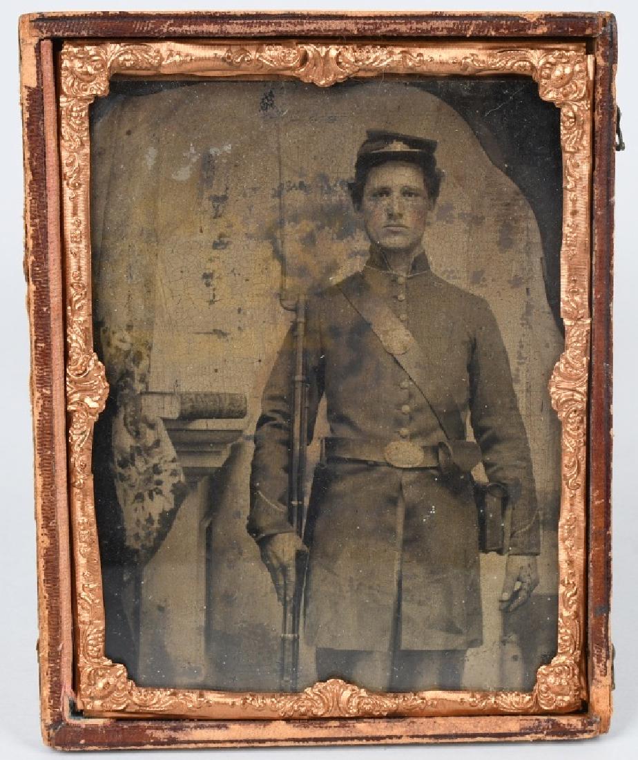 CIVIL WAR 1/2 PLATE TINTYPE ARMED UNION SOLDIER: 1/2 plate tintype of a Union soldier wearing a 9 button frock coat and standing at order arms with his rifle and fixed bayonet . His cartridge box and cap box are also visible. Image is housed in a 1/