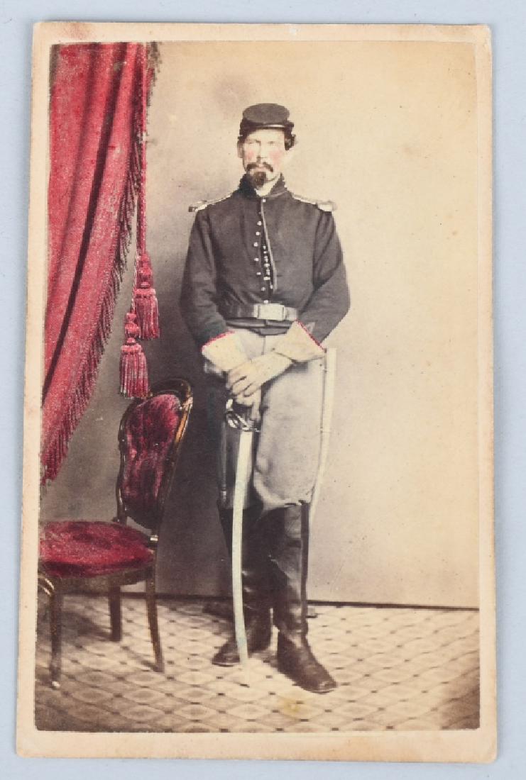 CIVIL WAR CDV ARMED ARTILLERY SOLDIER - TINTED: Beautifully tinted CDV featuring an armed artilleryman standing next to tinted red drapes and chair. He holds a cavalry saber and is wearing gauntlets that are tinted along the edge. excellent.
