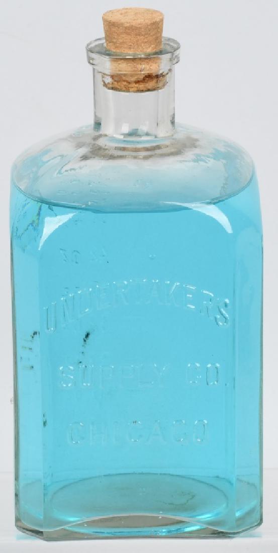 UNDERTAKERS SUPPLY CO. EMBALMING FLUID BOTTLE: Vintage bottle embossed "Undertakers Supply Co. Chicago" on obverse, and graduated ounce markings up to 64 ounces on reverse. Filled with colored water for display. 9 1/2" by 4 1/2" by 4 1/2". Excelle