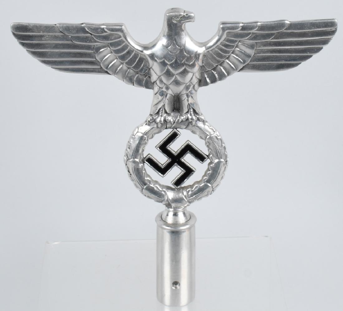 WWII NAZI GERMAN NSDAP POLITICAL FLAG POLE FINIAL: A polished aluminum flag pole finial in the form of an eagle whose outstretched wings have a span of 24cm and which clutches a wreathed mobile swastika in its talons. The obverse of the swastika is pa