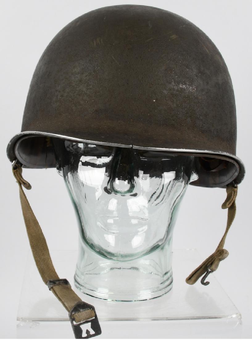 WWII US M1 FIXED BAIL COMBAT HELMET WITH LINER: Fixed bale mnganese shell. The shell retains almost all of its rough-textured olive drab paint to the exterior with some expected wear to its stainless steel rim. Chinstrap is complete. Liner is compl