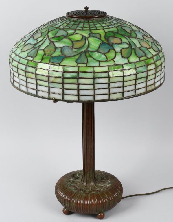 TIFFANY STUDIOS SWIRLING LEAF LEADED GLASS LAMP: Beautiful Tiffany Swirling Leaf Leaded Glass Lamp. Very nice 18" leaded glass shade in the Swirling Leaf style. Has typical broken panels. Very nice colors. Marked Tiffany Studios New York. Bronze Lib