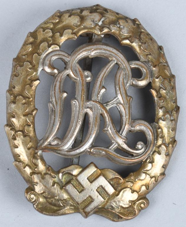 WWII NAZI GERMAN DRL SPORTS BADGE FOR WAR WOUNDED: The badge is in the form of a 1 7/8" tall vertical gilt oval oak leaf wreath with a mobile swastika and bow to its base encompassing the stylized silvered cut-out letters "DRL." To the reverse is a ve
