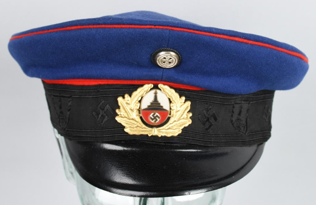 WWII NAZI GERMAN DRK B/NS RKB VISOR CAP: Dark blue wool top with red wool piping (to denote former Artillery service). The black rayon center band features machine embroidered mobile swastikas alternating with shields, within which are "Kyff