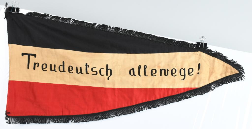 WWII NAZI GERMAN SCHOOL FLAG WITH FRINGE: WWII NAZI German period pennant measuring 29 X 15 inches and has the national colors black, white and red. flag is double sided with the text to the reverse Volksschule Mehlem and on the obverse Treud