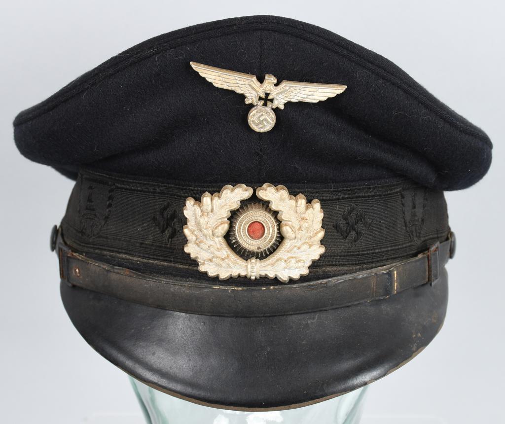 WWII NAZI GERMAN NS-RKB PERSONNEL'S VISOR CAP: A 1936 pattern deep navy blue wool construction visor cap. Fixed to the forward seam line of the body is a 1938 pattern stamped aluminum spread-winged eagle with a wreathed mobile swastika in its talo