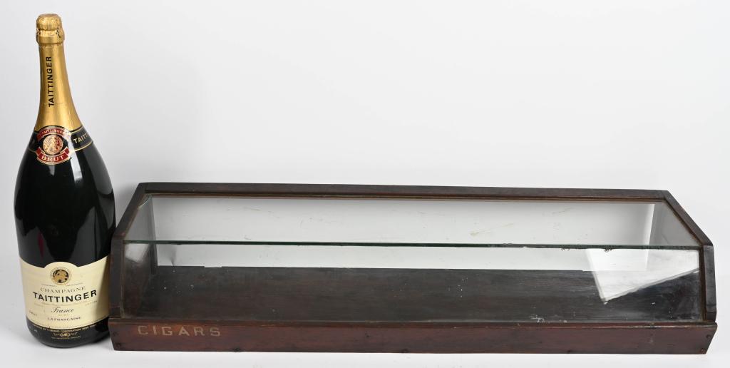 LOT CIGAR DISPLAY CASE & CHAMPAGNE DISPLAY BOTTLE: Cigar display case appears to be oak and is missing the back door. It measures 44" by 12". There is a crack in the corner of the top glass panel. The Taittinger Champagne bottle is plastic and measure