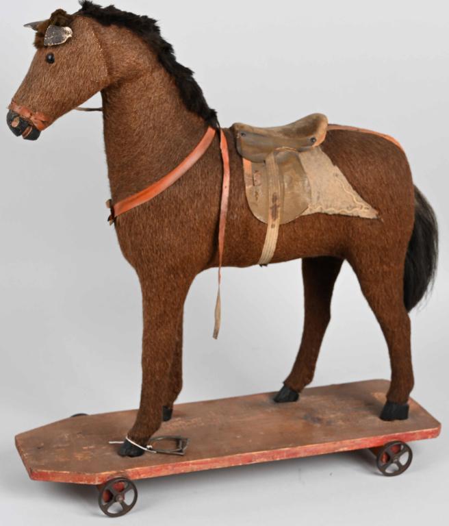 22" VICTORIAN HORSE ON PLATFORM: Wonderful hide covered horse with glass ete. Has sadle and bridle. Stands on wood platform with iron wheels. Still has both styrups. Nice early piece. 22" Excellent