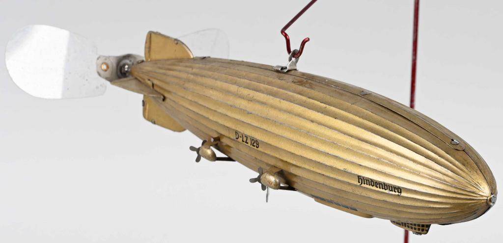 TIPP Tin Windup HINDENBURG ZEPPELIN: RARE tin windup Hindenburg Zeppelin made in Germany. Unusual version with no Nazi Swastikas on the tail fins. Very nice original toy. Windup works. Comes with modern metal display stand. 11" Excellent