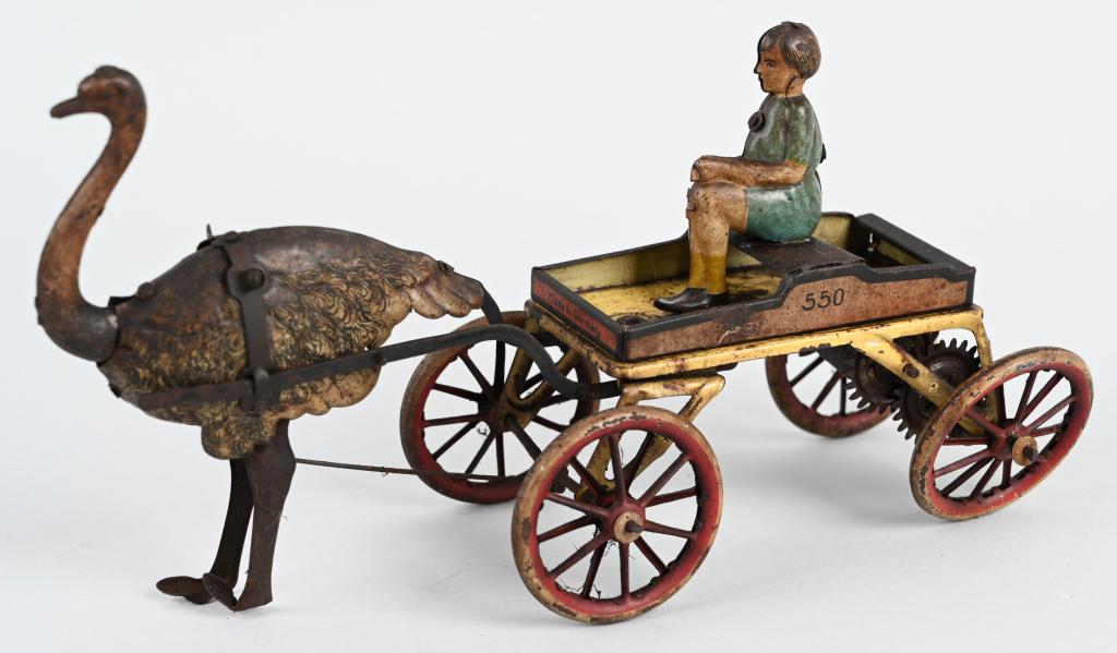 GNK TIN WINDUP OSTRICH CART: Tin windup Ostrich pulling cart with Rider. All original. Toy has aging throughout. Windup needs adjustment. 9 1/2" Very Good