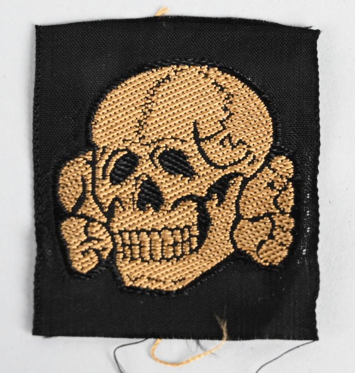 WWII NAZI GERMAN TROPICAL M41 / OVERSEAS CAP SKULL: BeVo, machine woven skull and cross bones in golden/tan rayon threads with black accent threads on a woven, black, rayon base. The skull features a bottom jaw, dual rows of teeth and nice eye, nose an