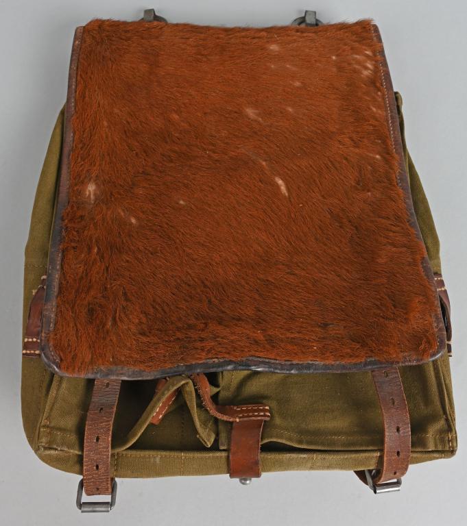 WWII NAZI GERMAN M34 PONY FUR BACKPACK COMPLETE: An olive drab canvas pack with leather and cowhide fittings, roughly 31cm wide, 39cm tall and 6cm deep, with a fold-over flap that covers its entire front. Decent fur coverage to the main flap. All th