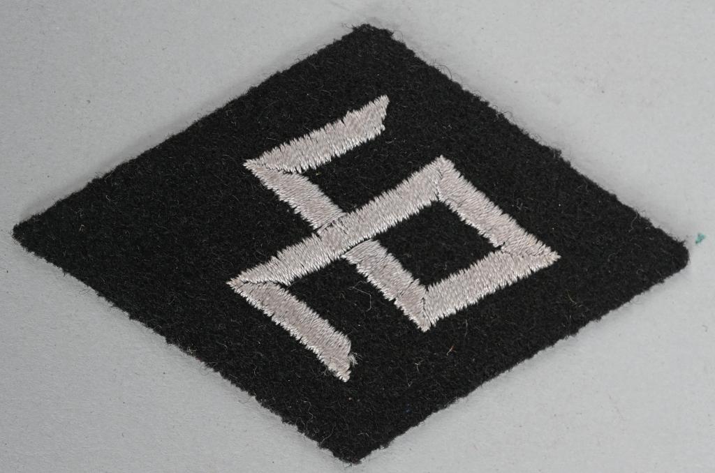 WWII NAZI SS RACE and RESETTLEMENT SLEEVE DIAMOND: WWII Nazi German EM/NCO SS Race and Resettlement Sleeve Diamond. A vertical, black wool diamond base featuring machine embroidered, Odal rune, indicating, Race and Resettlement , in silvery/gray rayon