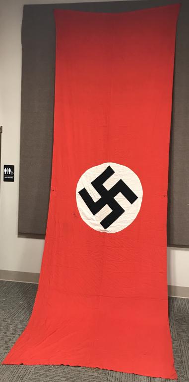 WWII NAZI GERMANY VEHICLE SINGLE SIDED FLAG WW2: Multi-piece cotton single sided construction banner approximately 60 x 194 inches. To its red field is a sewn white disk, with a printed mobile swastikas in black. Shows the expected period use and we