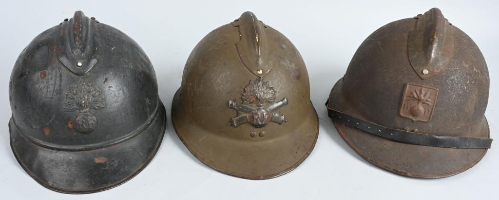3 FRENCH ADRIAN STYLE M26 COMBAT HELMETS: Lot of 3 French combat helmets. Adrian Style, all three have insignia on the front. One is green with an Artillery front plate, missing a liner. One has an ordnance insignia and "D.P." on the front, a