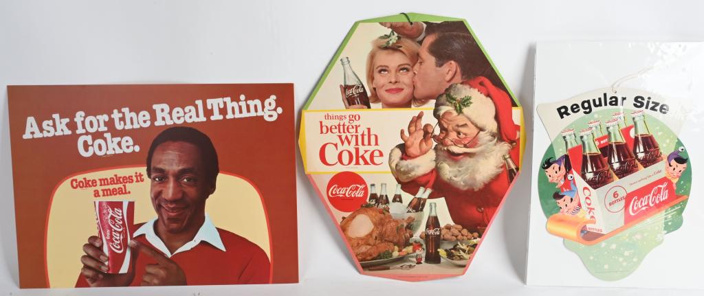 3- COCA COLA ADVERTISING SIGNS: Includes Bottle Topper with Elves, Santa Claus Double Sided Hanging Sign, and Bill Cosby Sign. Largest 17" Excellent