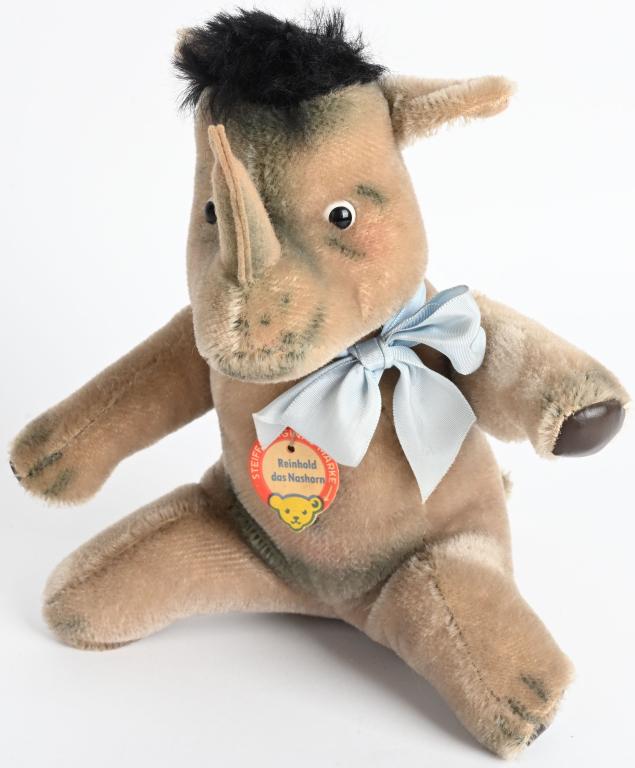 VINTAGE STEIFF REINHOLD RHINOCEROS: Has original paper chest tag and button. 8 1/2" high made of gray mohair, and horn is made of felt. Detailed head with google type eyes. Reinhold the Rhino was a popular character book created by Lori