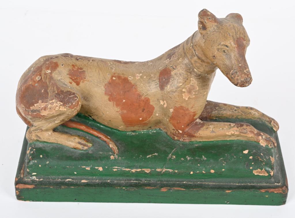 UNUSUAL PLASTER & WOOD RECLINING DOG FIGURE: Early plaster and wood Reclining Dog figure. Possibly used for advertising. Has original paint. Shows nice patina. 11" Very Good-Excellent From the James and Helen Berkheimer Collection