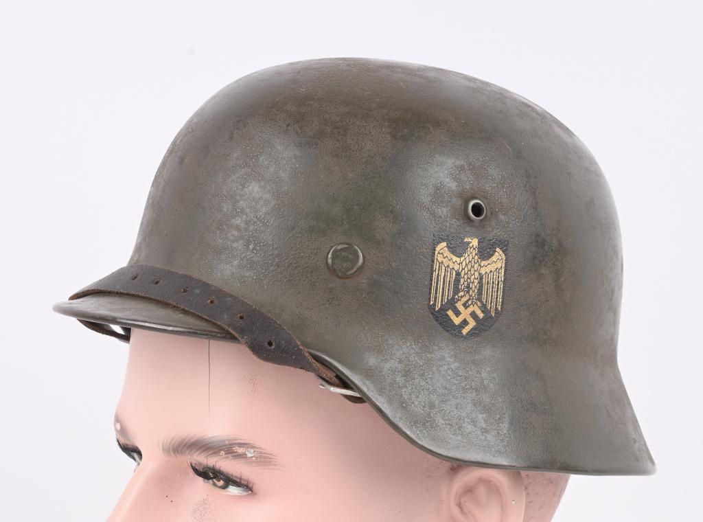 WWII NAZI GERMAN M35 DD WEHRMACHT COMBAT HELMET: The stamped, sheet steel construction helmet most of its original, green paint. The left side of the helmet has a Wehrmacht eagle shield decal which is retained 100%. The right side of the helmet has 