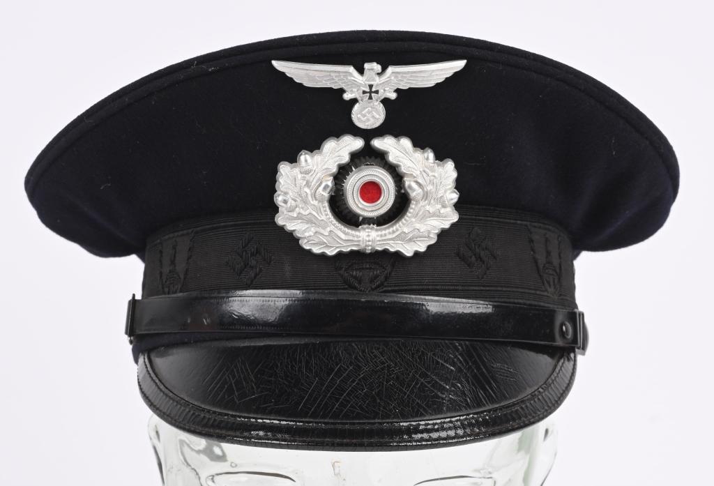 WWII NAZI GERMAN NSKOV VISOR HAT OR CAP WW2: A 1936 pattern, deep navy blue wool construction visor cap. Fixed to the forward seam line of the body is a 1938 pattern, stamped aluminum, spread-winged eagle with a wreathed, mobile swastika in its 
