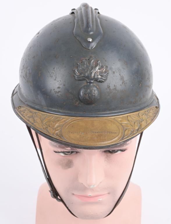 WWI FRENCH ADRIAN HELMET WITH VETERANS VISOR PLATE: Dark horizon blue paint finish showing wear in spots. Complete liner with chinstrap. Attached to the visor is a brass plate proclaiming the wearer to be a soldier of the Great War 1914-1918. The Chass