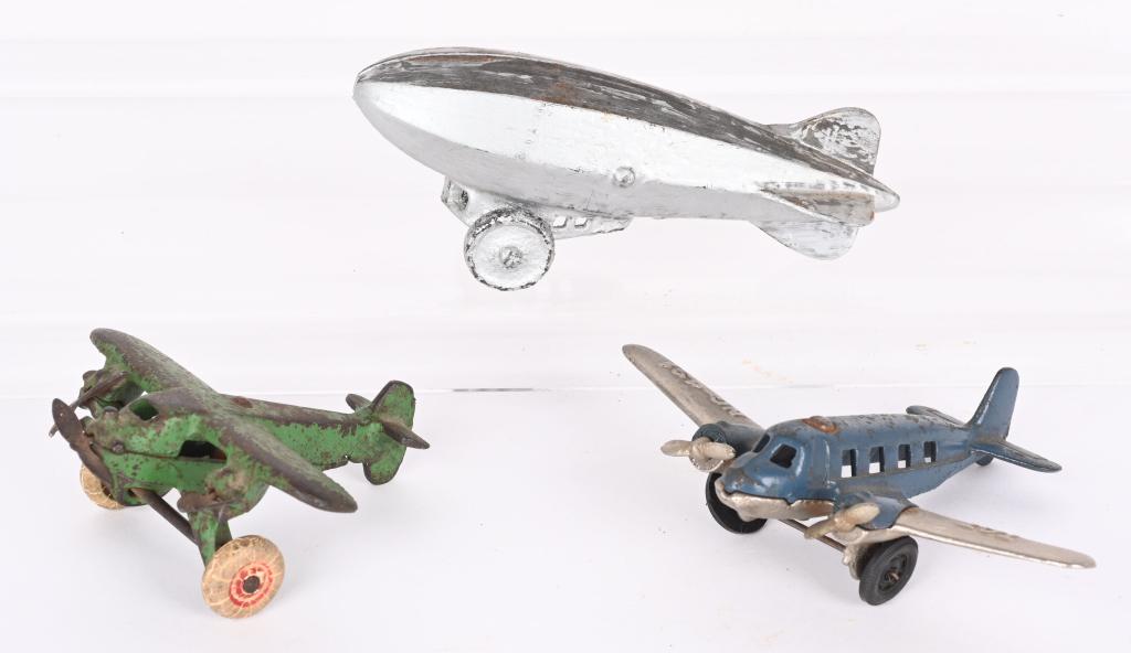 2- CAST IRON TOY AIRPLANES & ZEPPELIN: Lot includes a Arcade tri-motor monoplane, a Hubley TAT airplane, along with a Zeppelin. The Arcade is all original, the TAT is original with replacement wheels, and the Zeppelin is repainted. Largest