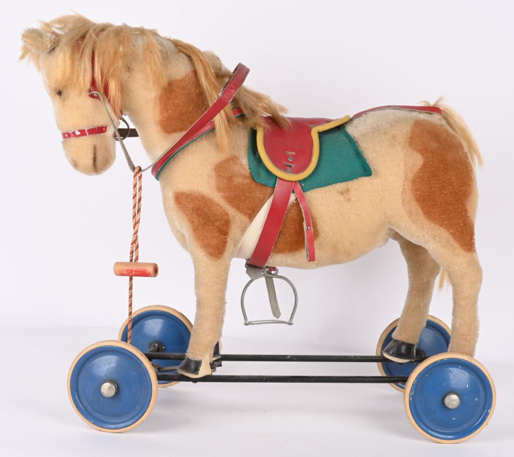 STEIFF LARGE RIDING HORSE ON WHEELS: Nice original Steiff large riding horse on wheels. Has button in ear. Nice colors and condition. Missing one stirrup. 25" L, 22" H. Very Good-Excellent