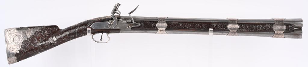 ELABORATE SILVER OVER UNDER FLINTLOCK BLUNDERBUSS: Outstanding silver mounted Over under superimposed flintlock blunderbuss. With duckbill pattern muzzles measuring 1 3/8 wide by 1" diameter. Unique double ignition pan design that allows the operator 