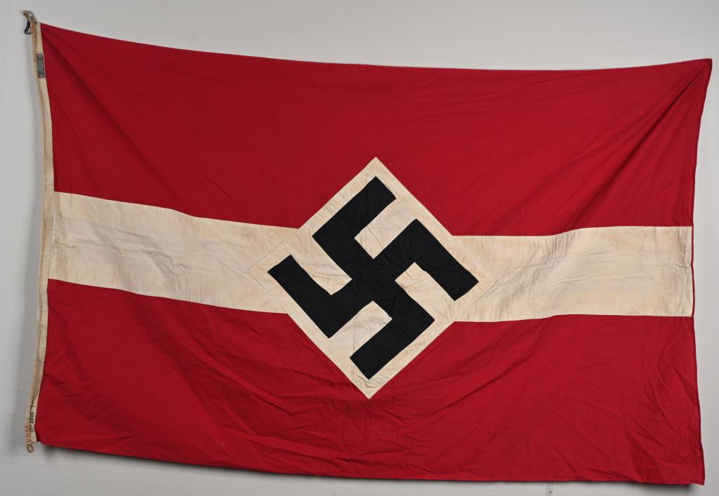 WWII NAZI GERMAN HITLER YOUTH FLAG W/ TAG WW2: Multi-piece construction flag to either side of whose 120cm x 210cm red field is sewn a central horizontal white band against the center of which to each side are sewn approximately square white diamo
