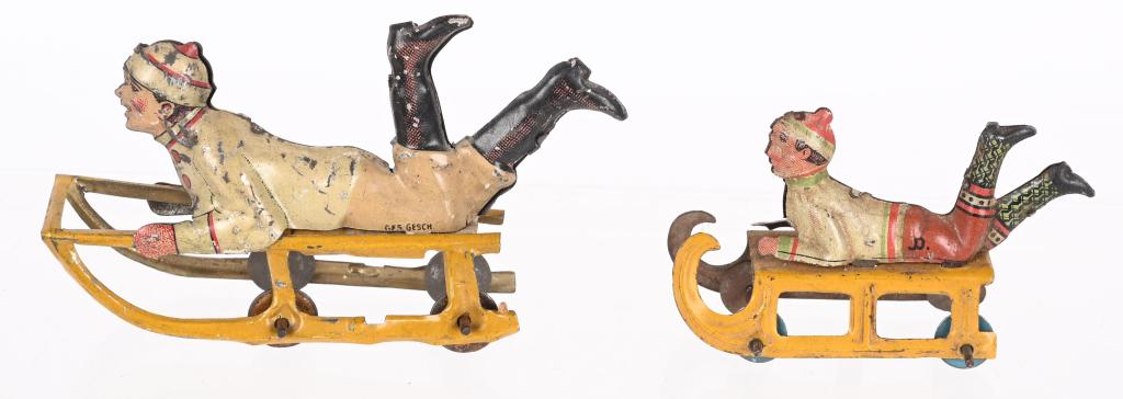 2- GERMAN PENNY TOY BOYS ON SLEDS: Pair of German Penny Toy Boys on Sleds. Both with nice details. Largest 3 1/2" Excellent