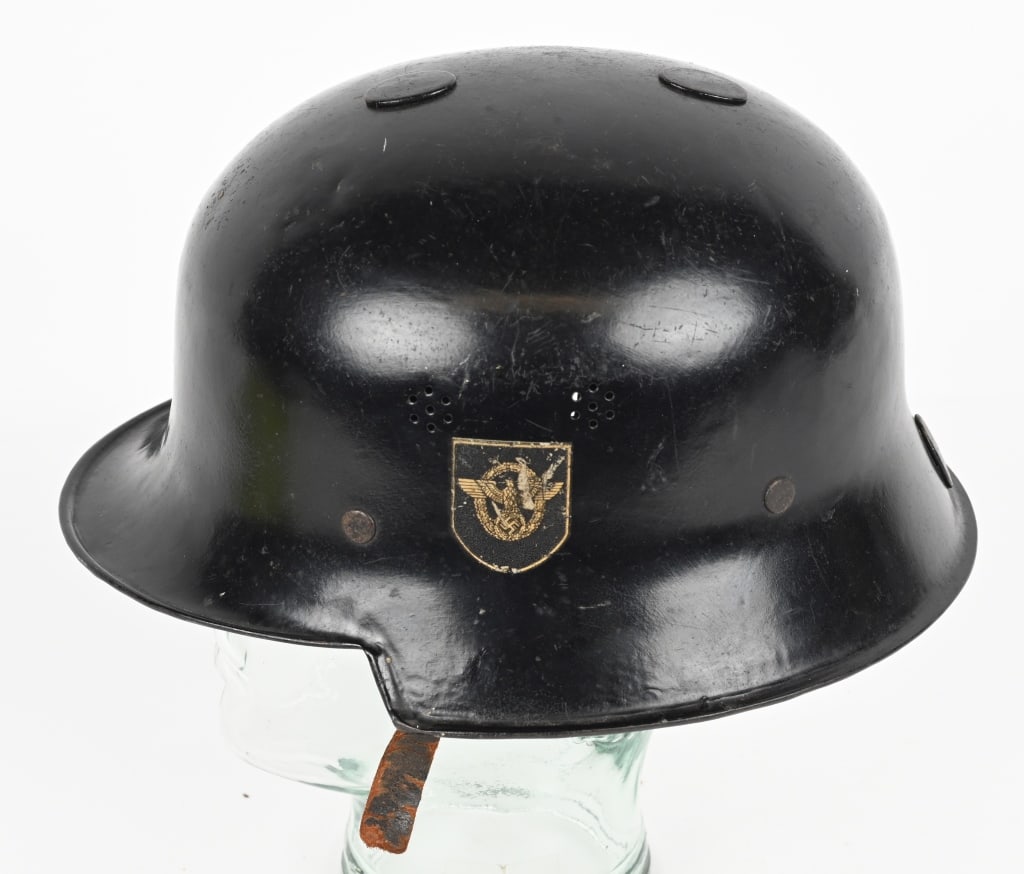 WWII NAZI M34 FEUERSCHUTZPOLIZEI HELMET W LINER: The stamped, sheet steel construction helmet retains a good portion of its original black paint. The left side of the helmet has a silver bordered, black based, police decal with the second pattern, s