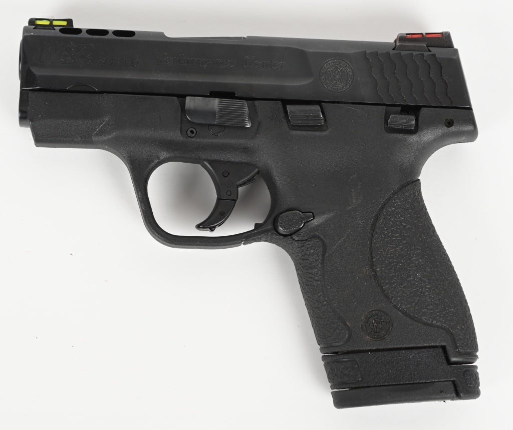SMITH & WESSON M&P 9 SHIELD PERFORMANCE CENTER: SERIAL NUMBER: HXV9092. BARREL: 3". CALIBER: 9MM LUGER. MANUFACTURED: 2010's. Performance center logo on the slide. Fiber optic front sight and U-notch rear. Matte blued slide and black polymer frame.