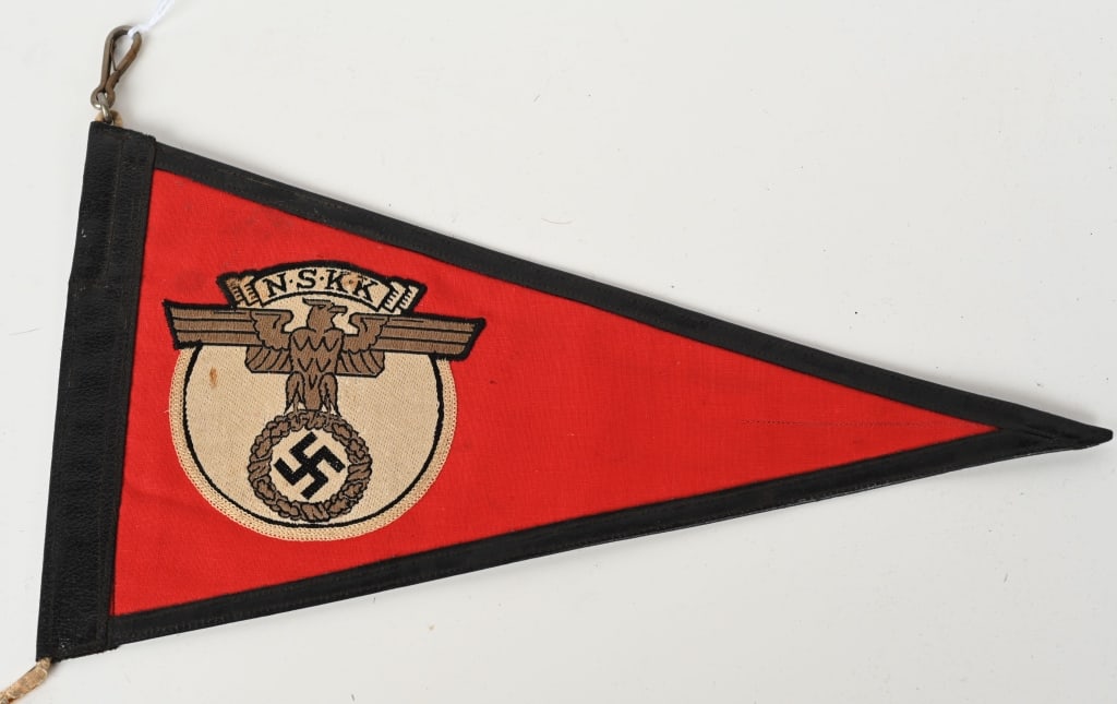 WWII NAZI GERMAN NSKK CAR PENNANT WW2: A multi-piece cotton construction pennant, 31cm across with a 17cm tall hoist edge. Sewn to both sides of its red field is a 85mm diameter white disk, upon which is machine woven a copper-colored, spr