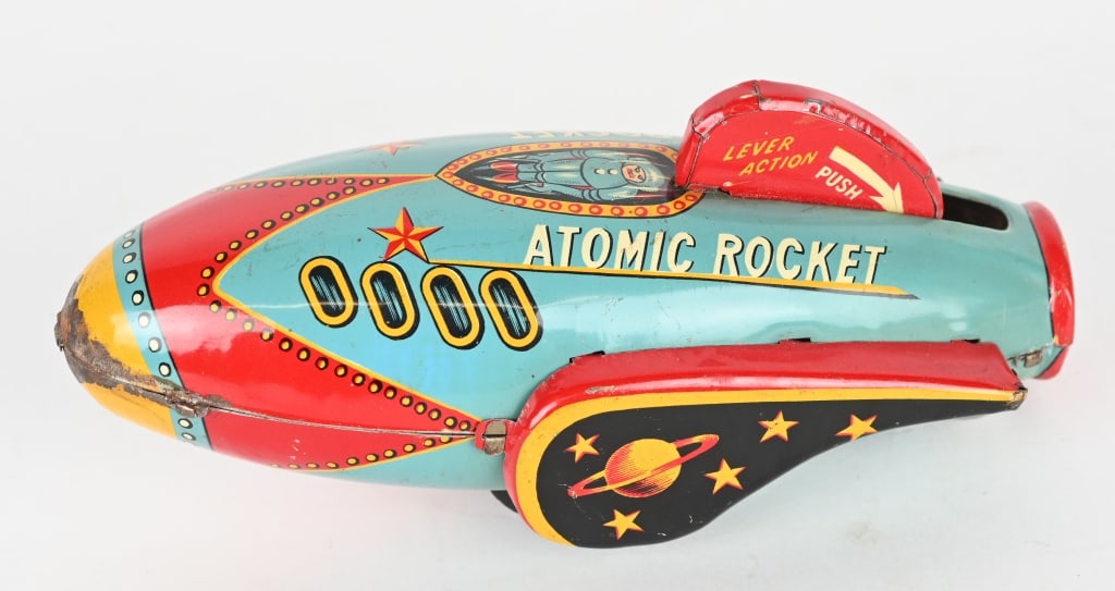 JAPAN TIN FRICTION ATOMIC ROCKET: All original with great colors and graphics. Has unusual; push tailfin down to wind the toy. Works good. A very scarce Space Toy. 6 1/2" Excellent