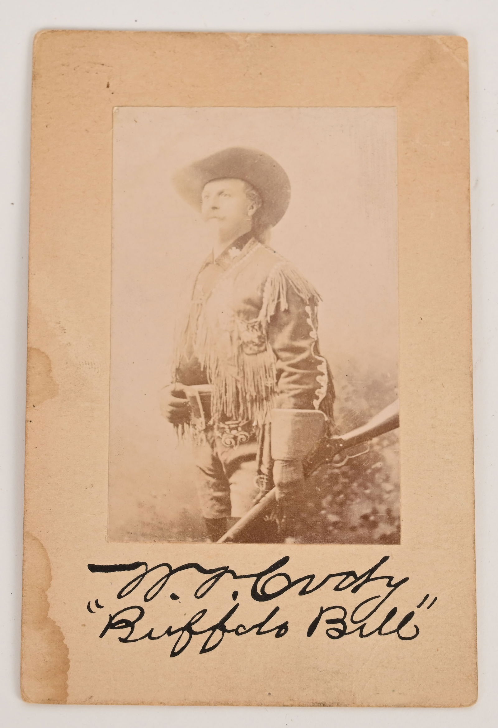 Autographed Photograph of Buffalo Bill Cody: Buffalo Bill Cody in his fringed jacket with his rifle in hand. 2 3/4 x 3 1/2 inch photo mounted on a 3 1/2 x 5 inch card. Signed "W.F. Cody 'Buffalo Bill'". Small stain lower left. William Frederick