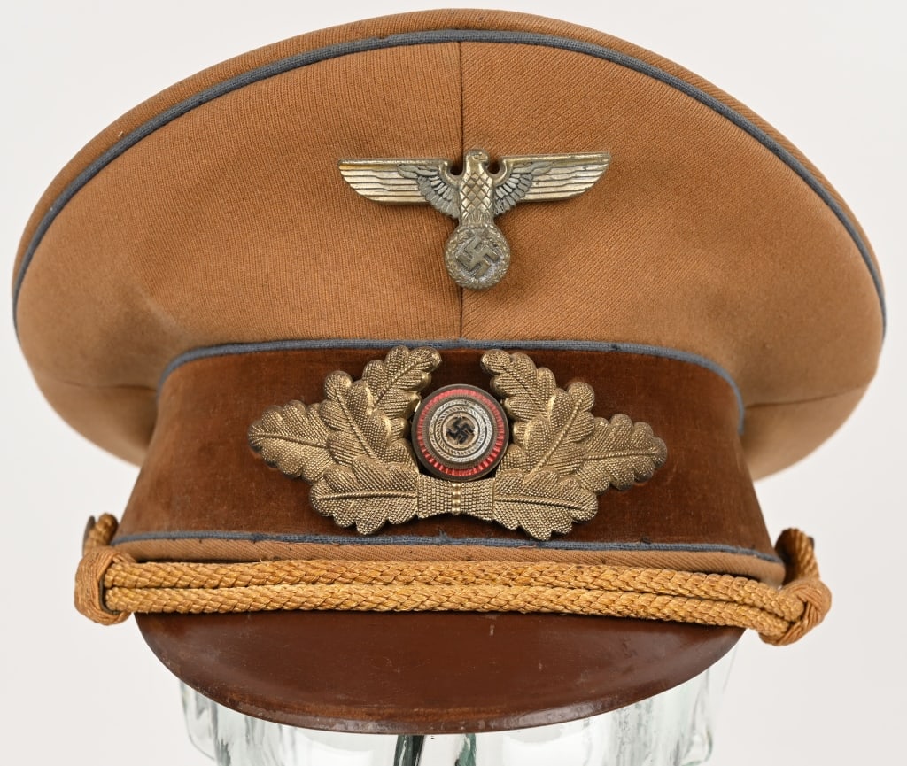 WWII ORTS LEVEL NSDAP POLITICAL LEADER'S VISOR CAP: A 1939 pattern tan-colored, fine whipcord-weave, wool/rayon construction visor cap. The cap features a one-piece circular crown, piped in blue, a body with seams to each of its cardinal points, a one-