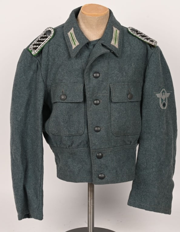 WWII NAZI M44 COMBAT POLICE ISSUE SERVICE TUNIC: An issued M44 combat policer service tunic. Late-war model made from typical blue-green feldgrau colored wool. Complete with all factory applied buttons. The tunic retains both BeVo sleeve eagle and c