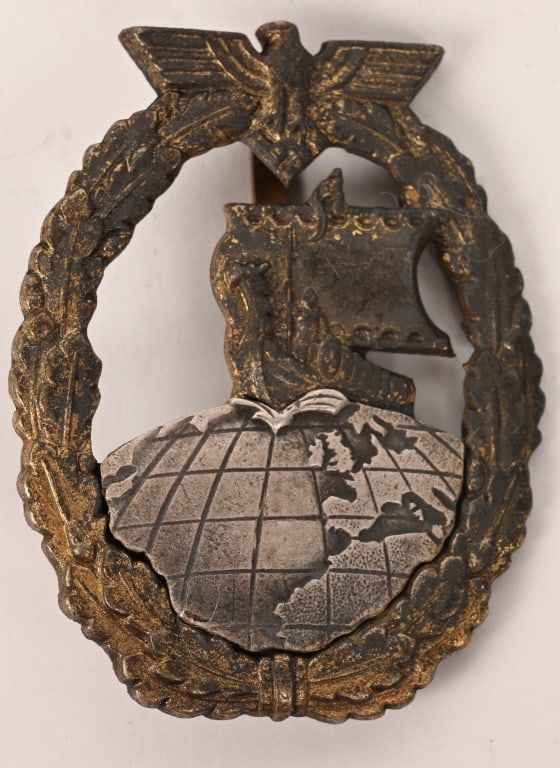 WWII NAZI GERMAN KM AUXILIARY CRUISER WAR BADGE: Two piece, die struck, tombak construction badge with fire gilt and nickel/silver plated finishes. The badge is in the form a gilt washed, vertically oval, embossed, oak-leaf wreath with a national ea