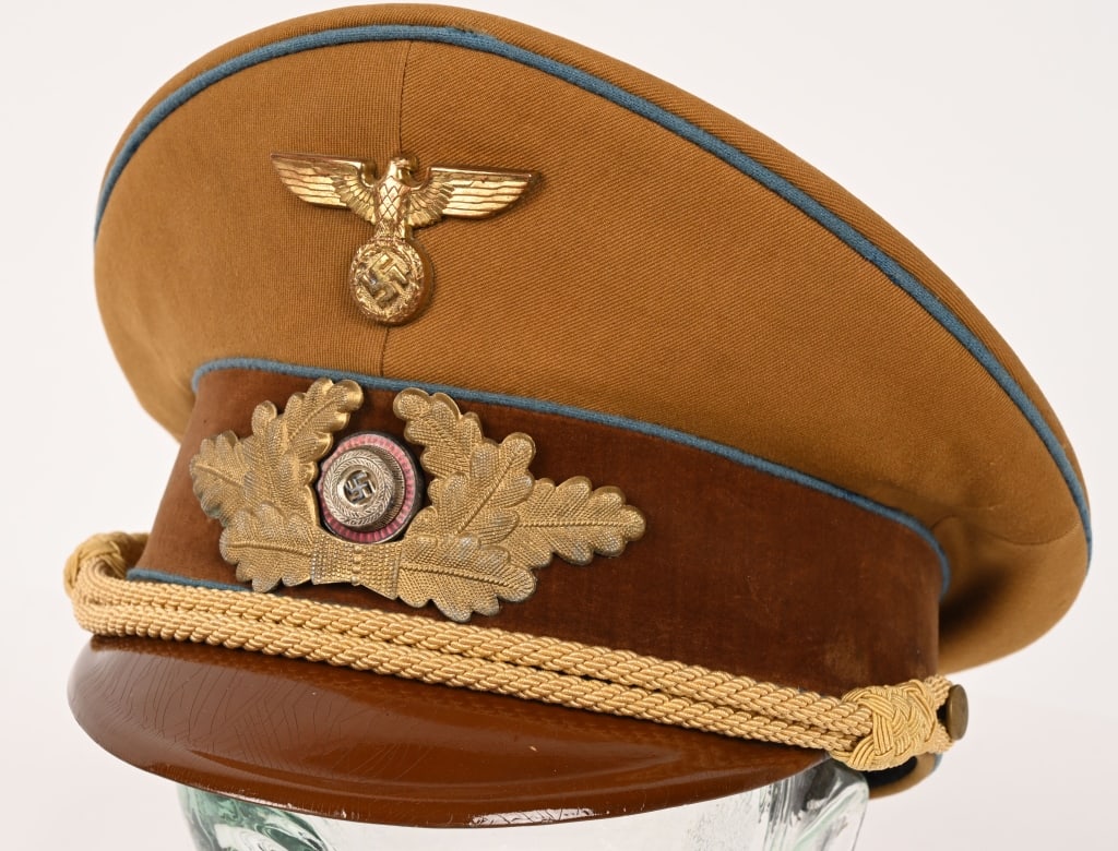 WWII ORTS LEVEL NSDAP POLITICAL LEADER'S VISOR CAP: A 1939 pattern tan-colored, fine whipcord-weave, wool/rayon construction visor cap. The cap features a one-piece circular crown, piped in blue, a body with seams to each of its cardinal points, a one-