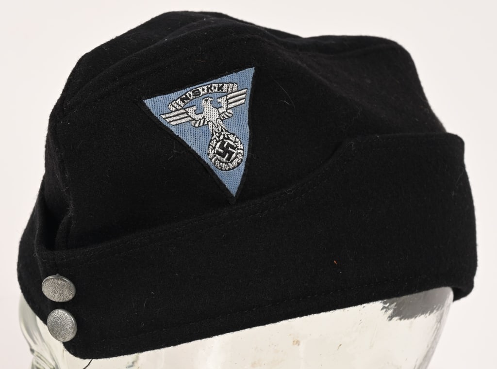 WWII NAZI GERMAN NSKK MOTOR BRIGADE HOCHLAND CAP: Black wool cap whose fold-down side panels slope towards the front where they are sewn to the side of the cap. Sewn to the left side of the cap above where its side panel begins to slope is a machine