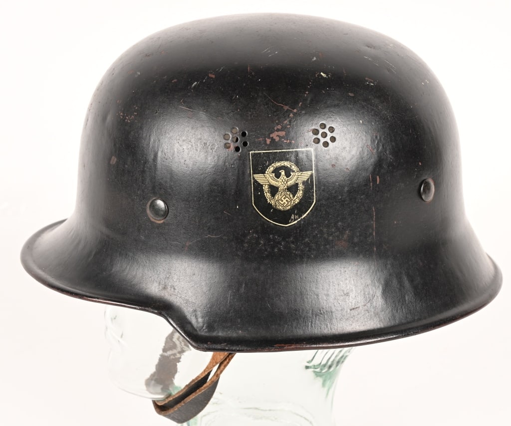NAZI M34 DOUBLE DECAL FEUERSCHUTZPOLIZEI HELMET: The stamped, sheet steel construction civic M34 helmet retains most of its original black satin finish paint. The left side of the helmet has a silver bordered black based police decal with the second
